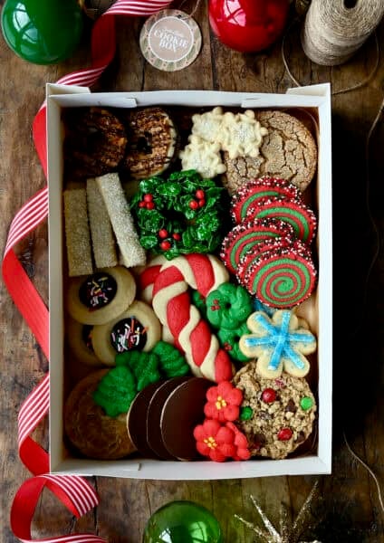 A holiday cookie box packed with several different kinds of Christmas cookies, including candy cane sugar cookies, Christmas monster cookies, thumbprint cookies, Cornflake wreaths, spritz cookies and molasses cookies.