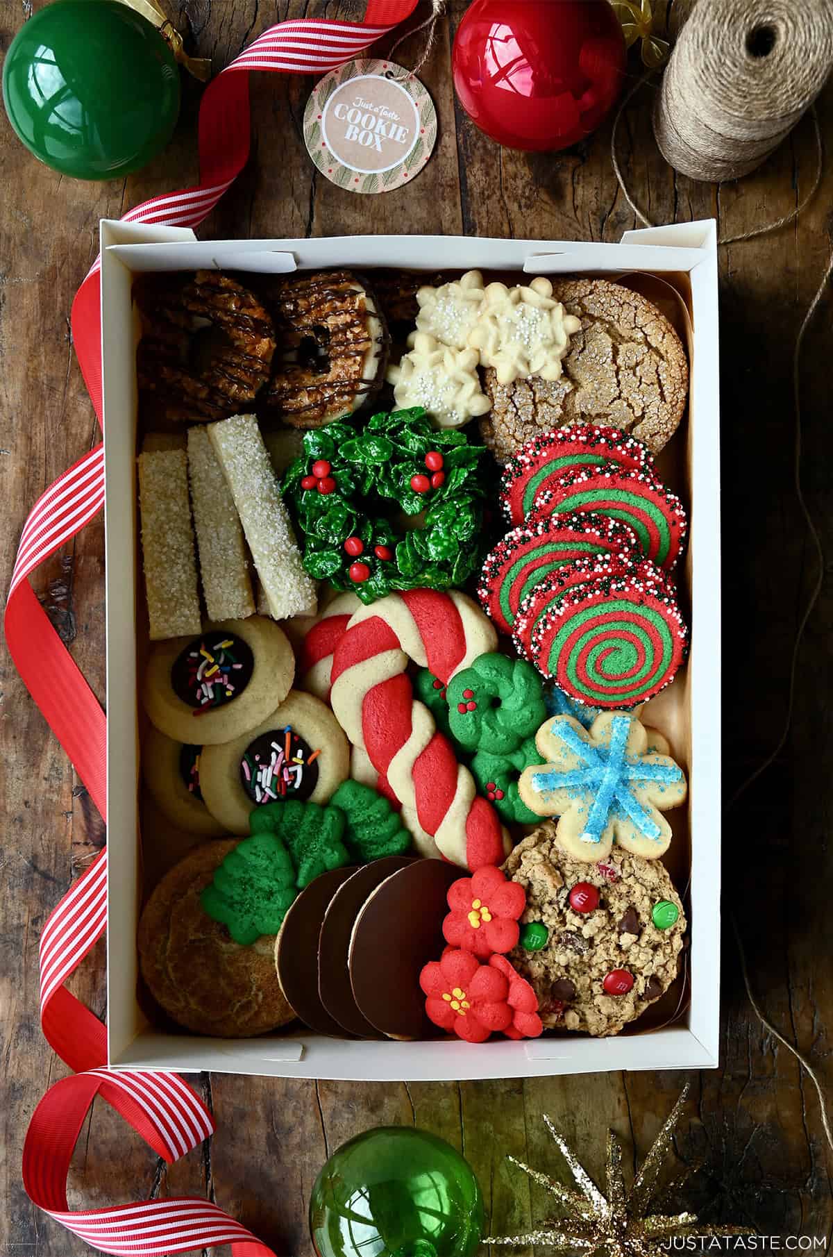 A holiday cookie box packed with several different kinds of Christmas cookies, including candy cane sugar cookies, Christmas monster cookies, thumbprint cookies, Cornflake wreaths, spritz cookies and molasses cookies.