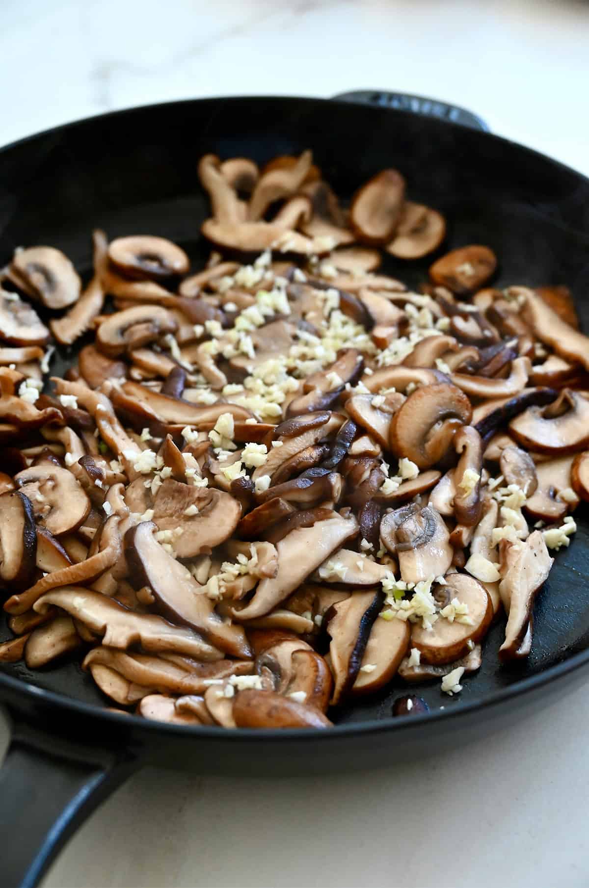 Sautéed mushrooms in a large skillet with minced garlic.