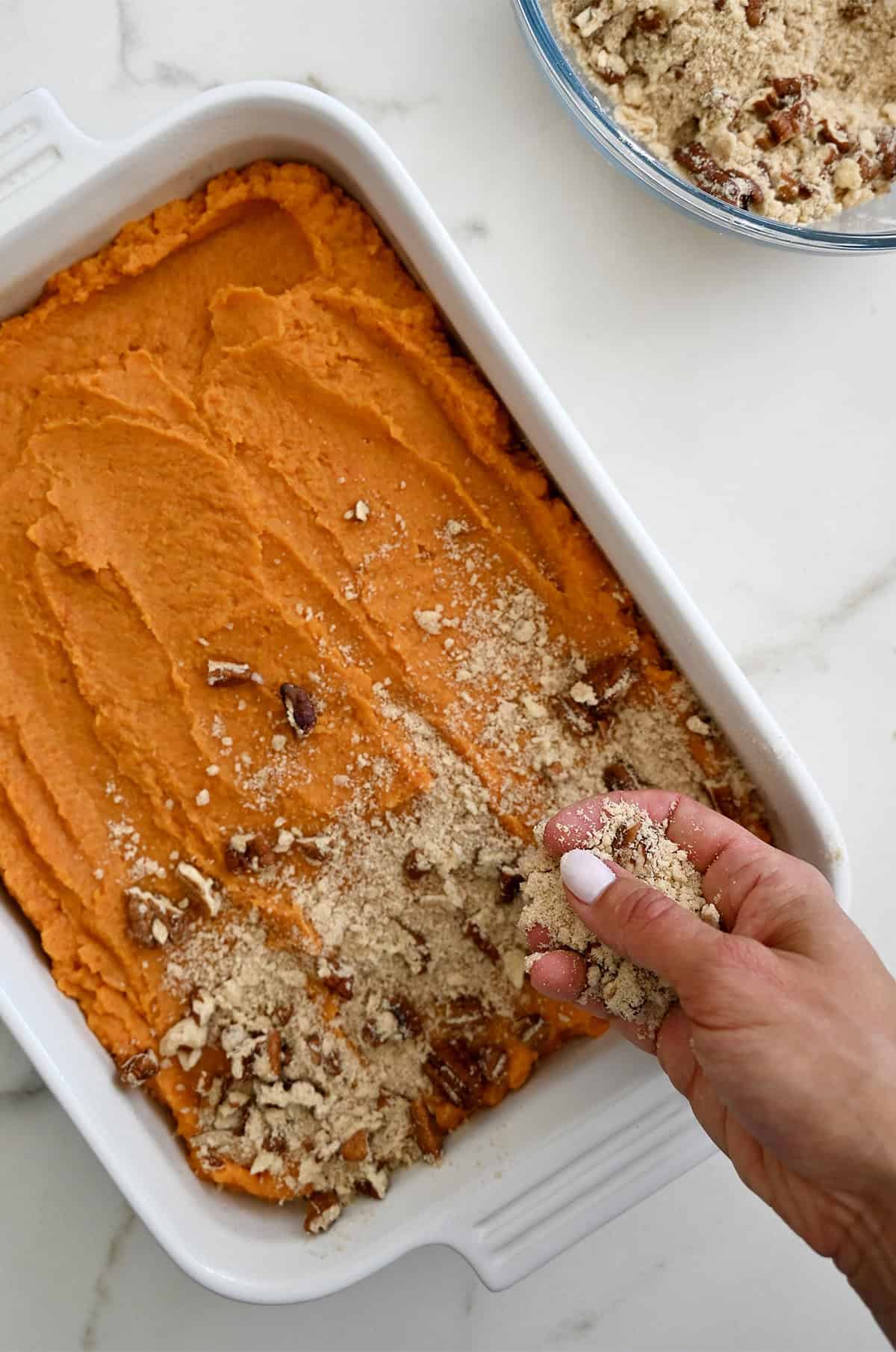 Sprinkling a pecan topping over a creamy sweet potato mixture in a 9x13 baking dish.