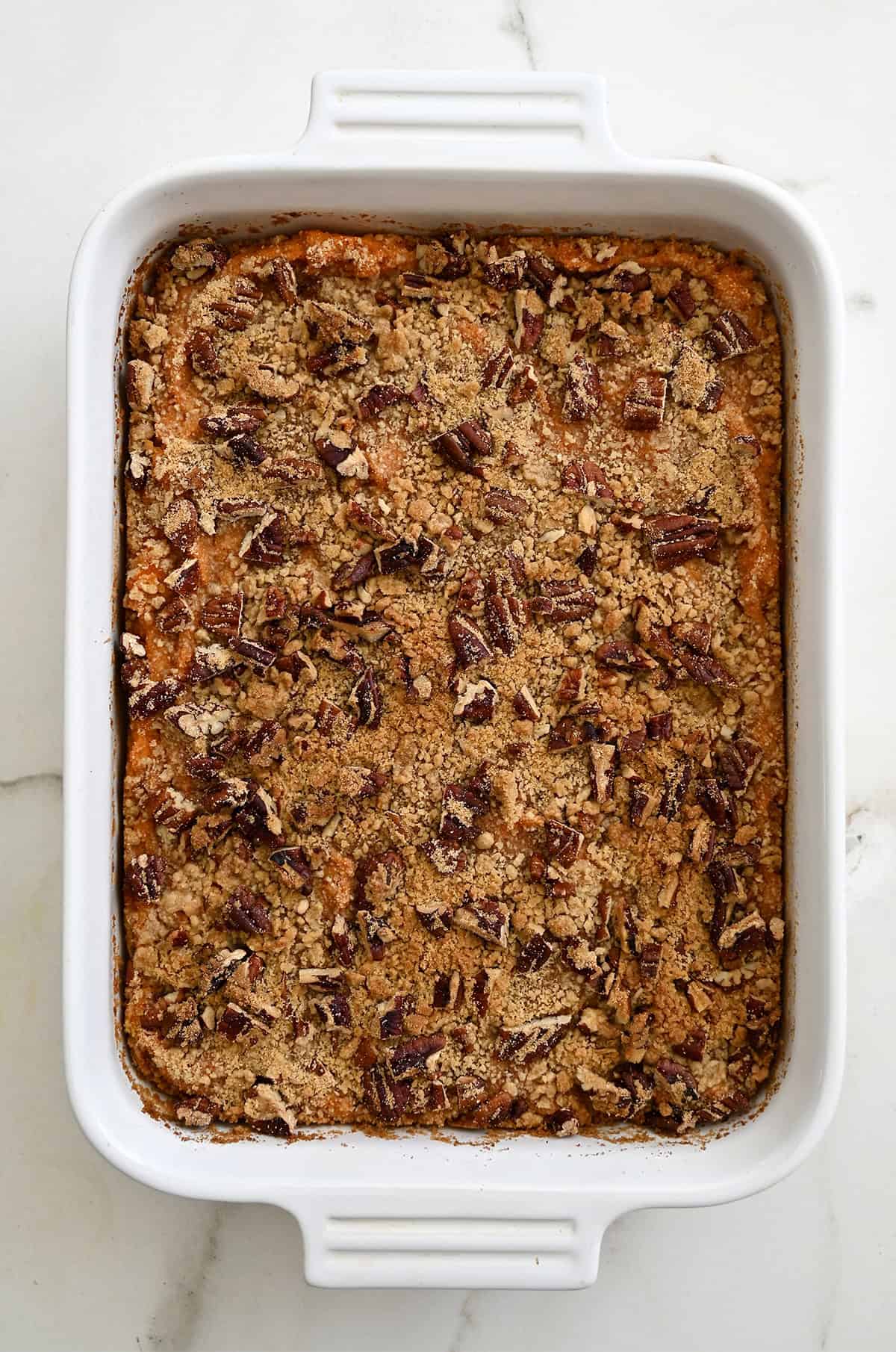 Baked sweet potato casserole with a golden brown pecan crumble in a white baking dish.
