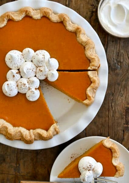 Homemade pumpkin pie topped with dollops of whipped cream and sprinkled with pumpkin pie spice in a deep pie dish.