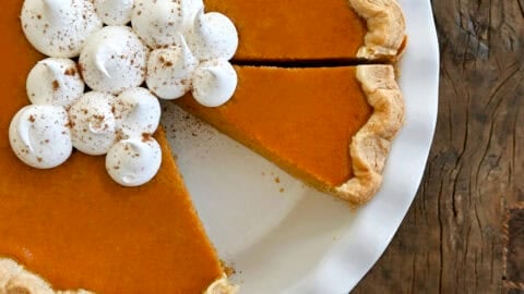 Homemade pumpkin pie topped with dollops of whipped cream and sprinkled with pumpkin pie spice in a deep pie dish.