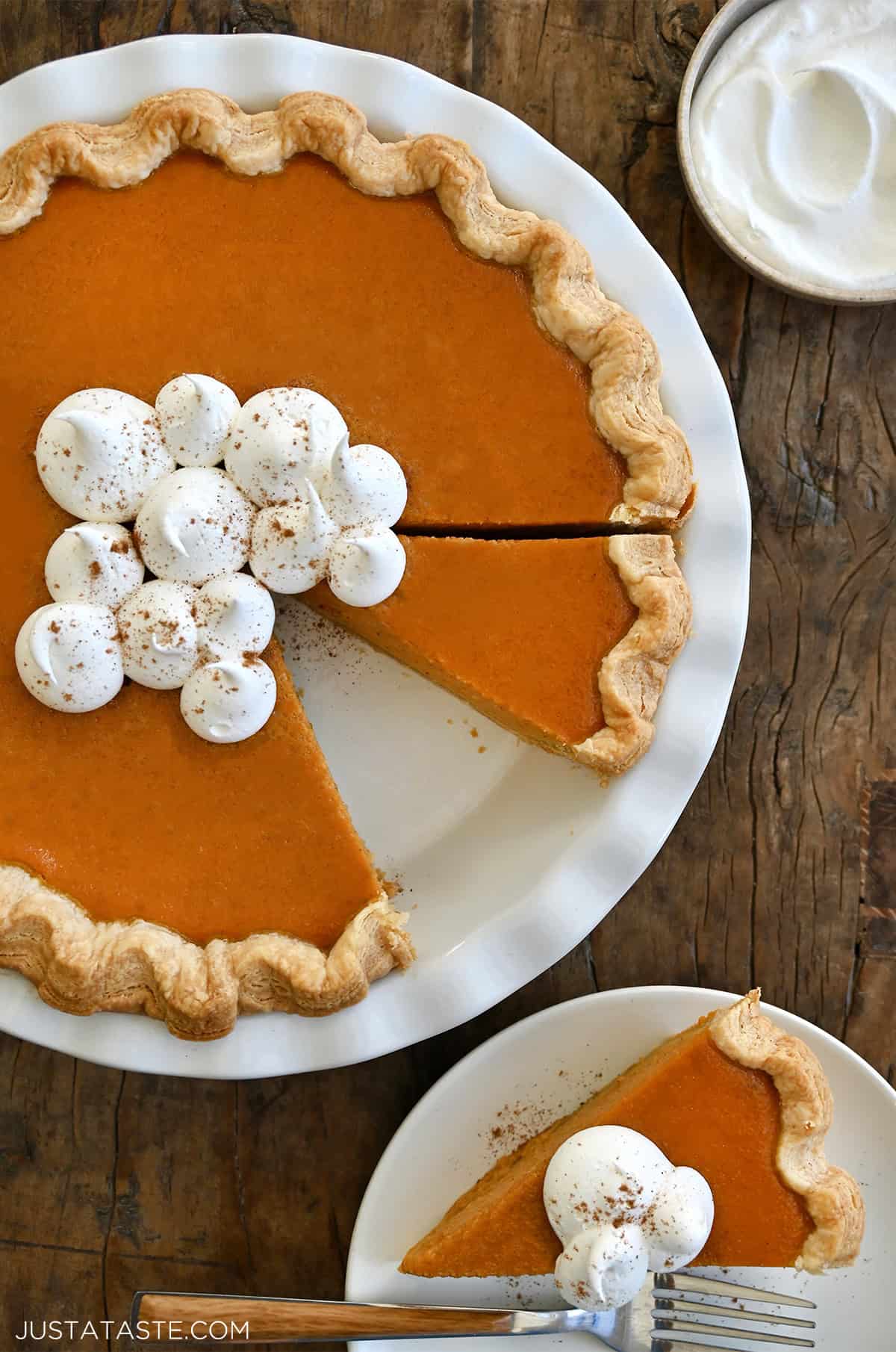 Homemade pumpkin pie topped with dollops of whipped cream and sprinkled with pumpkin pie spice in a deep pie dish.