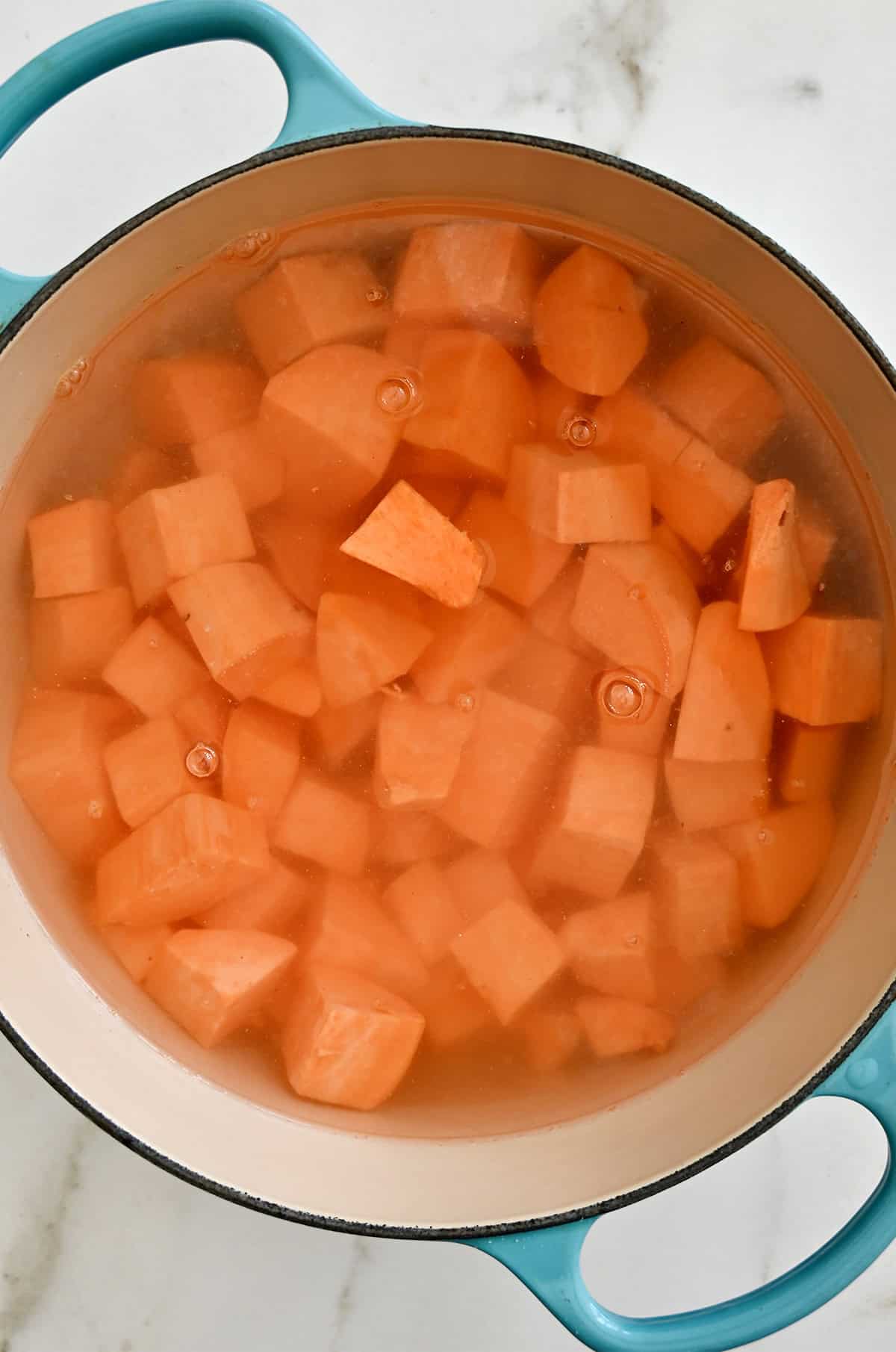 Diced sweet potatoes are boiling in a large pot of water.