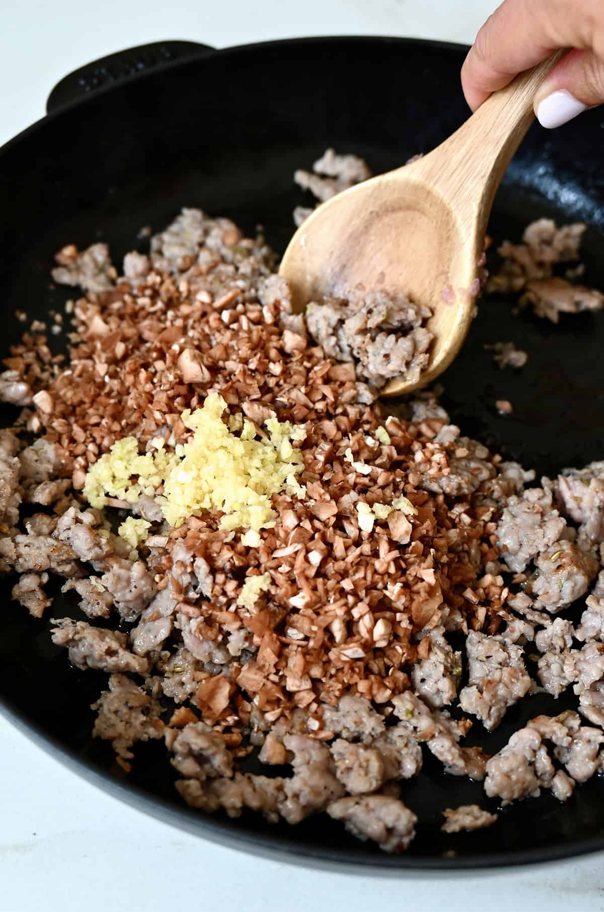 Cooked sausage in a skillet with chopped mushroom stems and minced garlic.