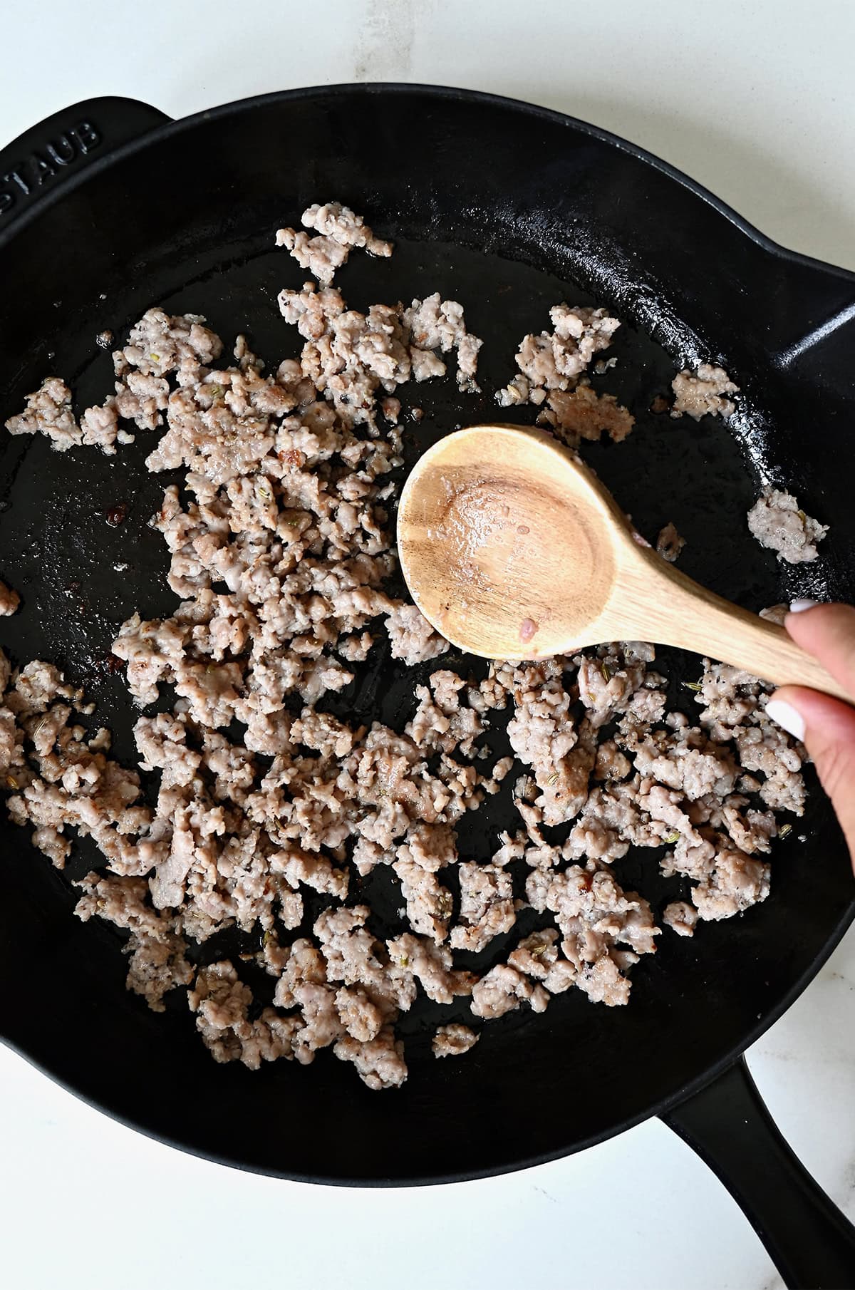 Browned Italian sausage in a skillet being stirred with a wooden spoon.
