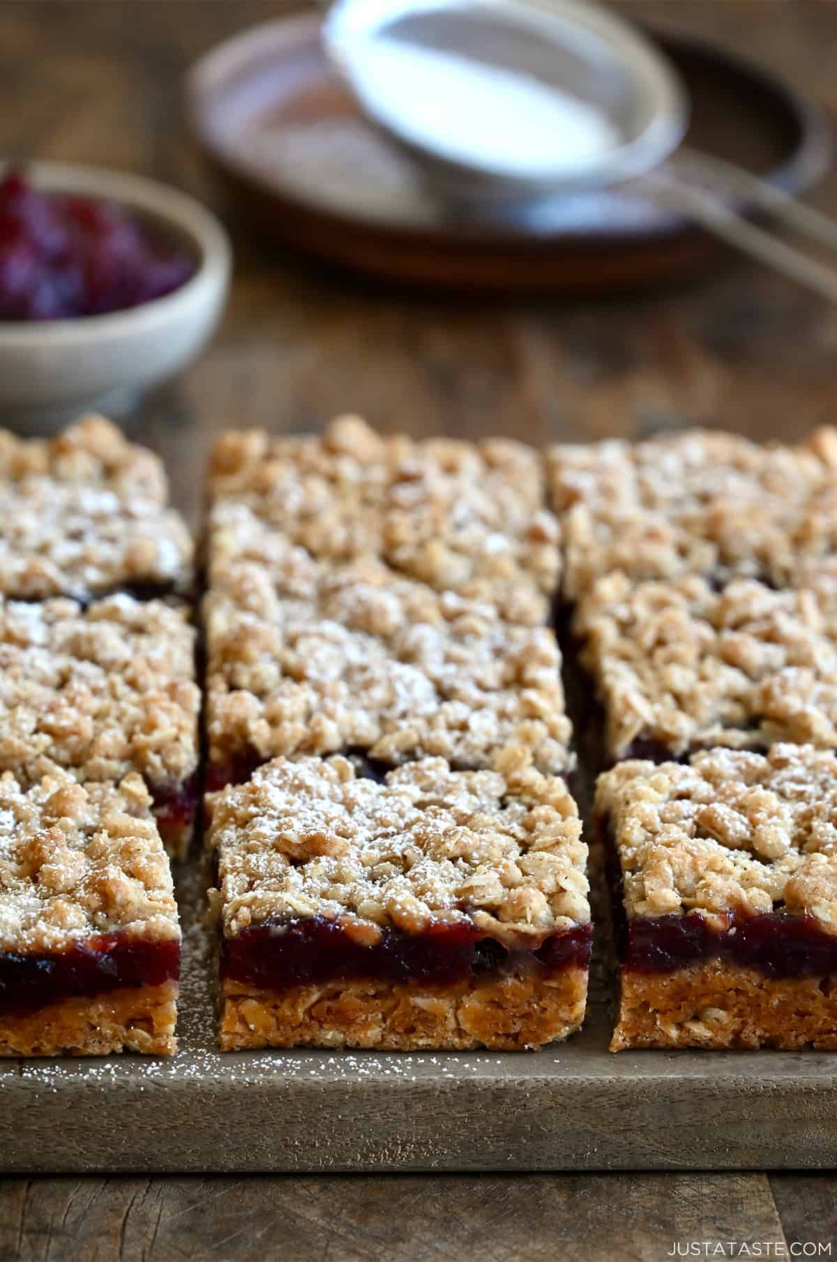 Squares of cranberry shortbread bars dusted with powdered sugar on a glass cutting board.
