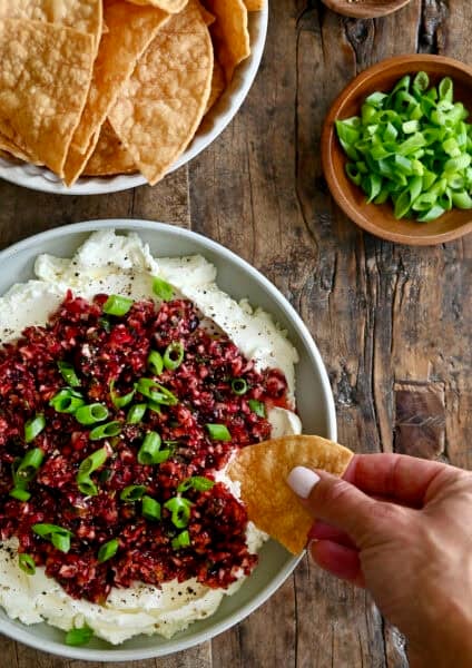 Cream cheese topped with a cranberry jalapeño relish being dipped into with a chip.