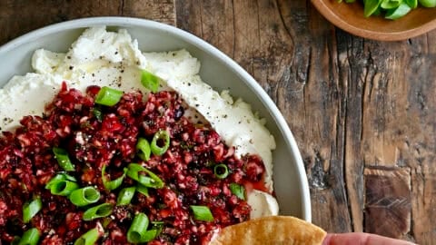 Cream cheese topped with a cranberry jalapeño relish being dipped into with a chip.