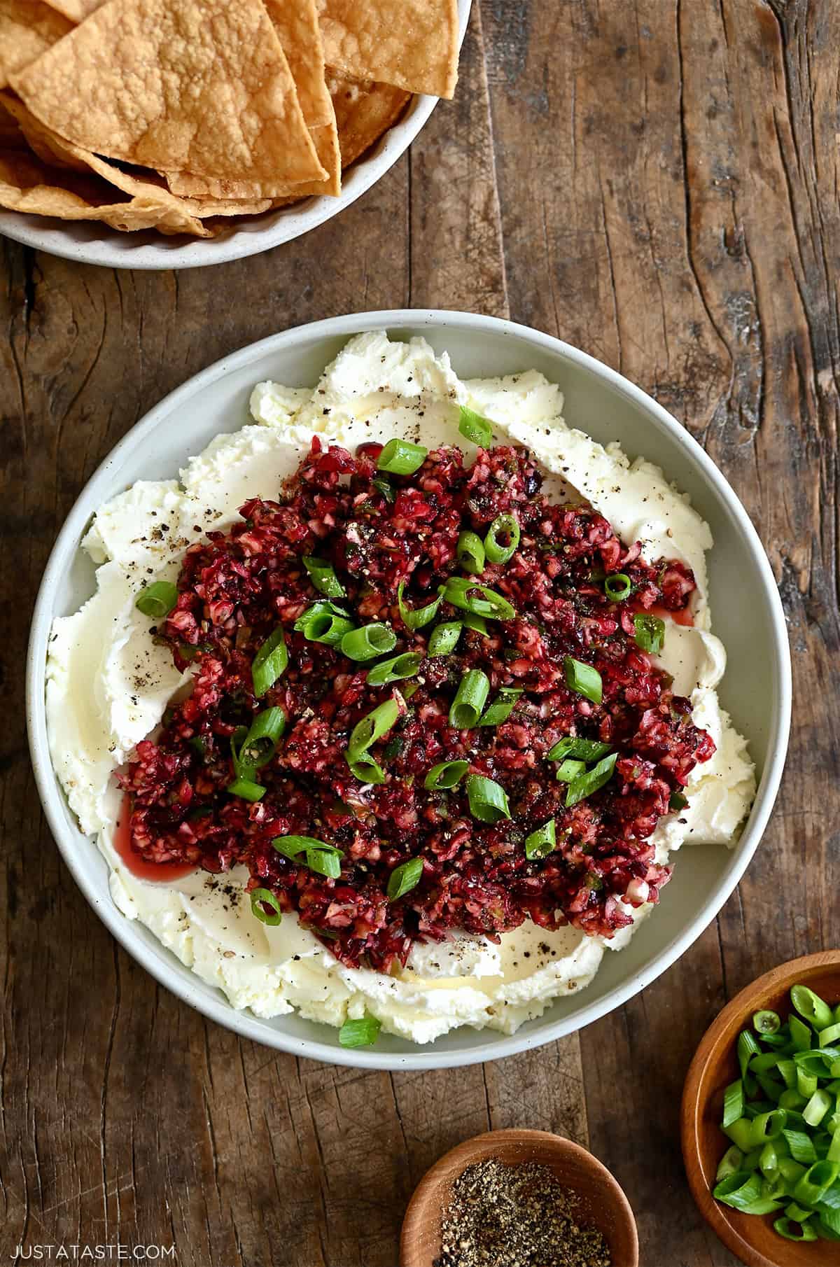 Cranberry jalapeño relish over cream cheese on a serving plate garnished with chopped scallions, salt and pepper.