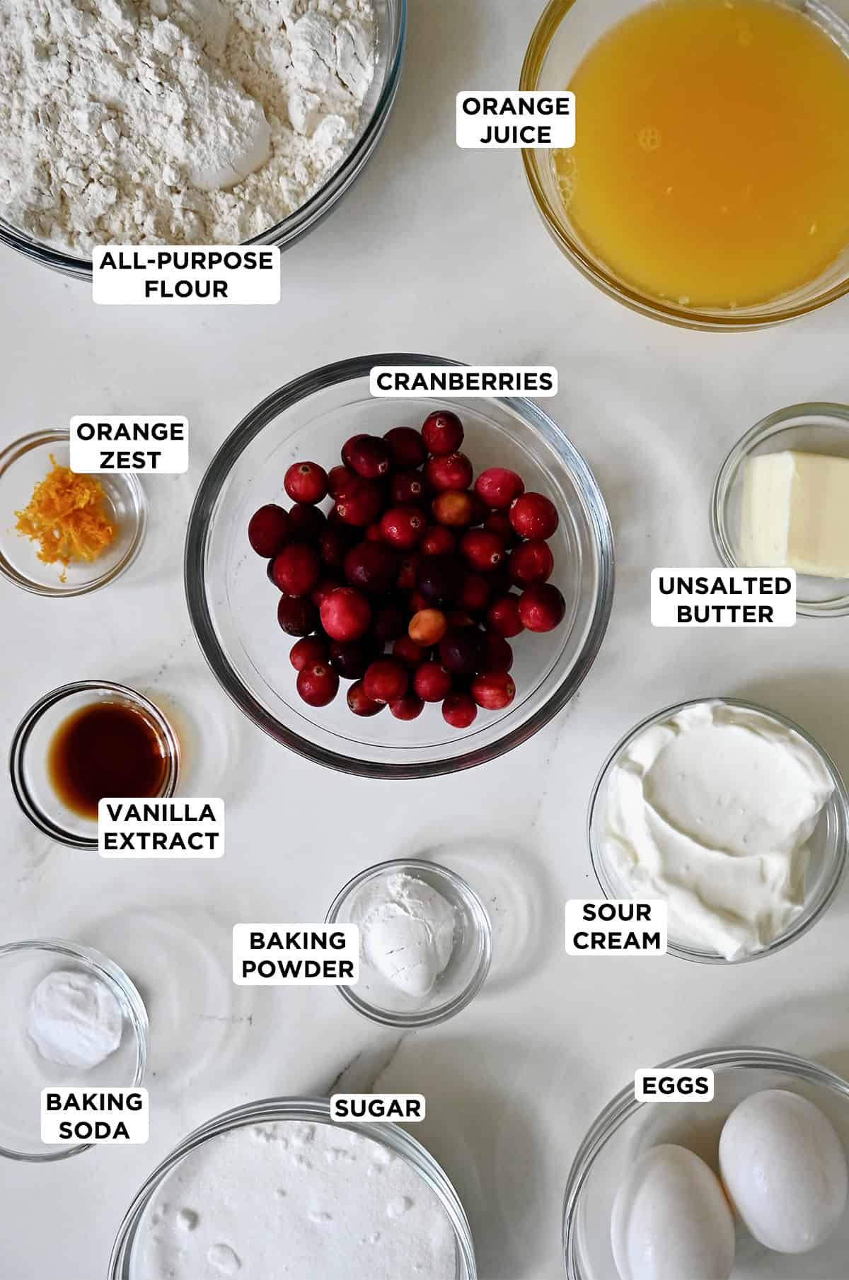Ingredients to make cranberry orange muffins in various sizes of glass bowls.