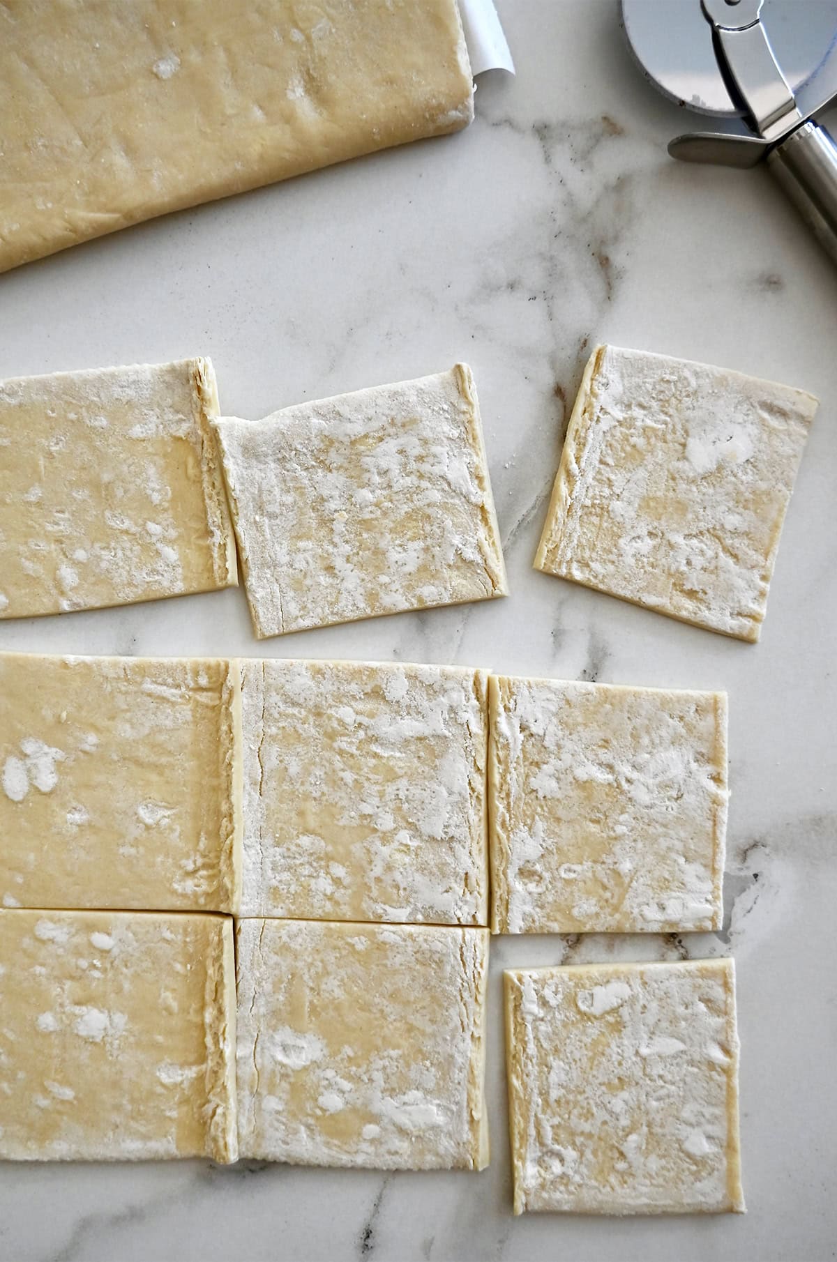 Sluoksniuotos tešlos lakštas, supjaustytas į devynis kvadratus ant lengvai miltais pabarstyto darbinio paviršiaus.