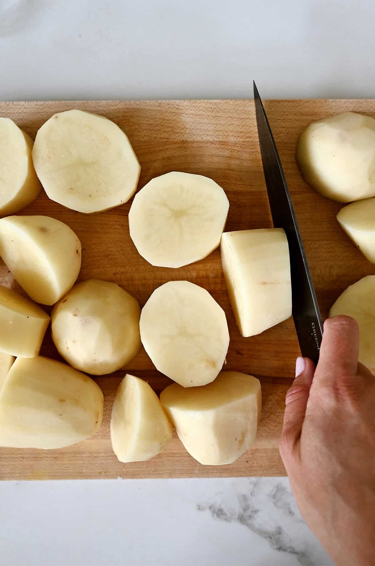 Peeled potatoes cut into quarters on a cutting board.