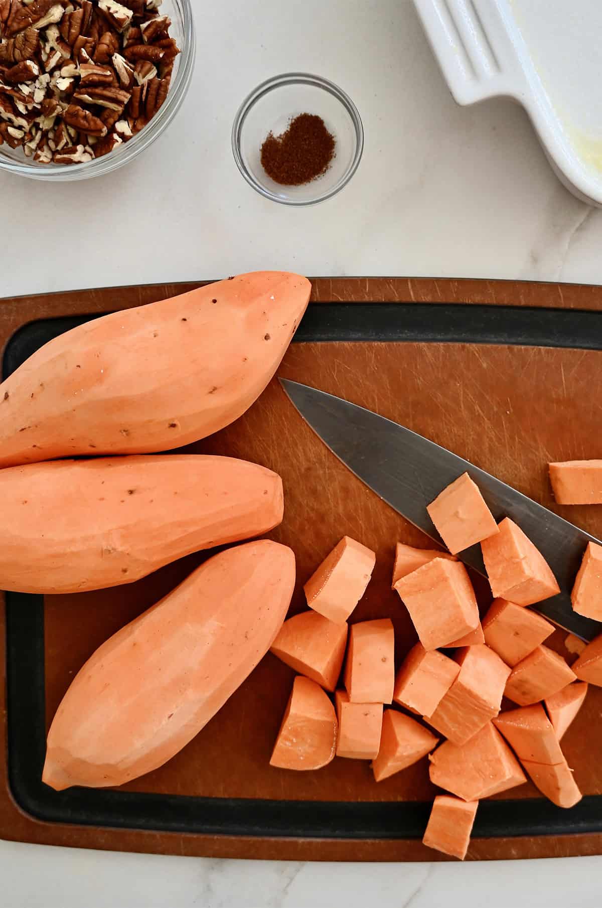 Cut up sweet potatoes on a cutting board with a sharp knife.