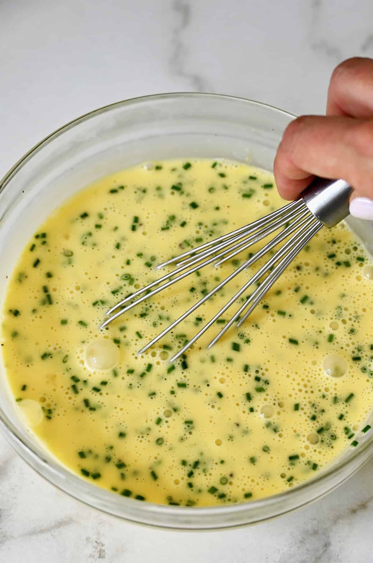 Stikliniame dubenyje išplakti kiaušinius ir smulkintus laiškinius česnakus.