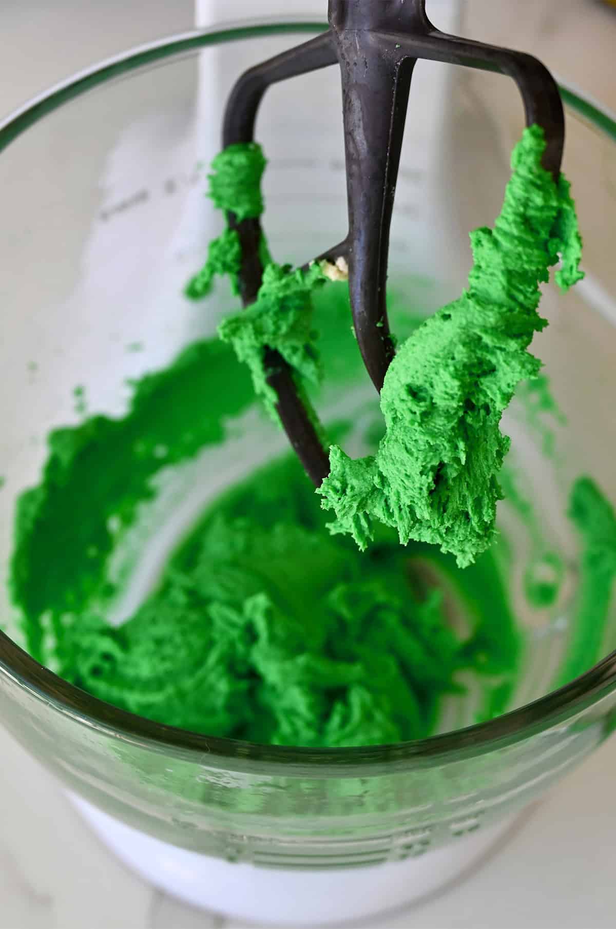 Green colored spritz cookie dough in a stand mixer.