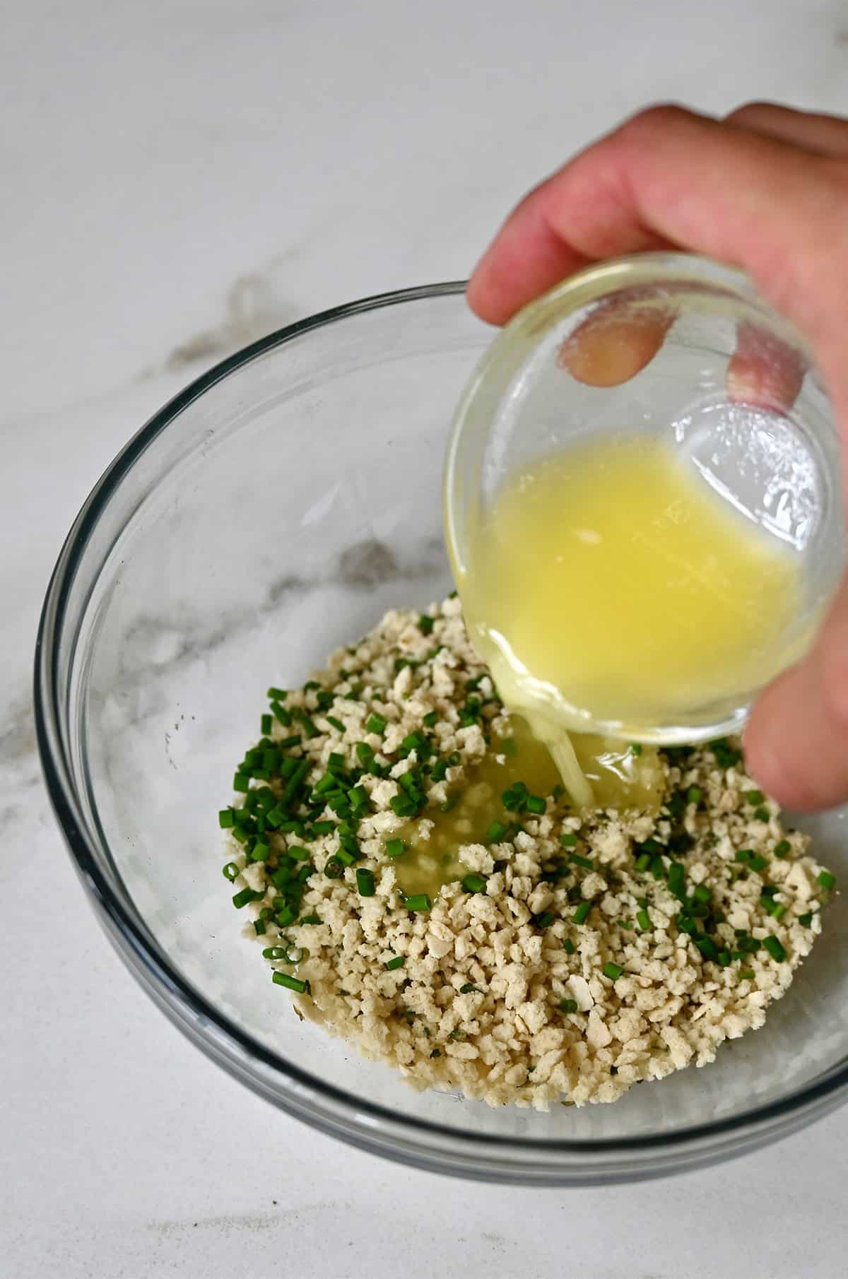 Adding melted butter to a bowl with Panko breadcrumbs and chopped chives.
