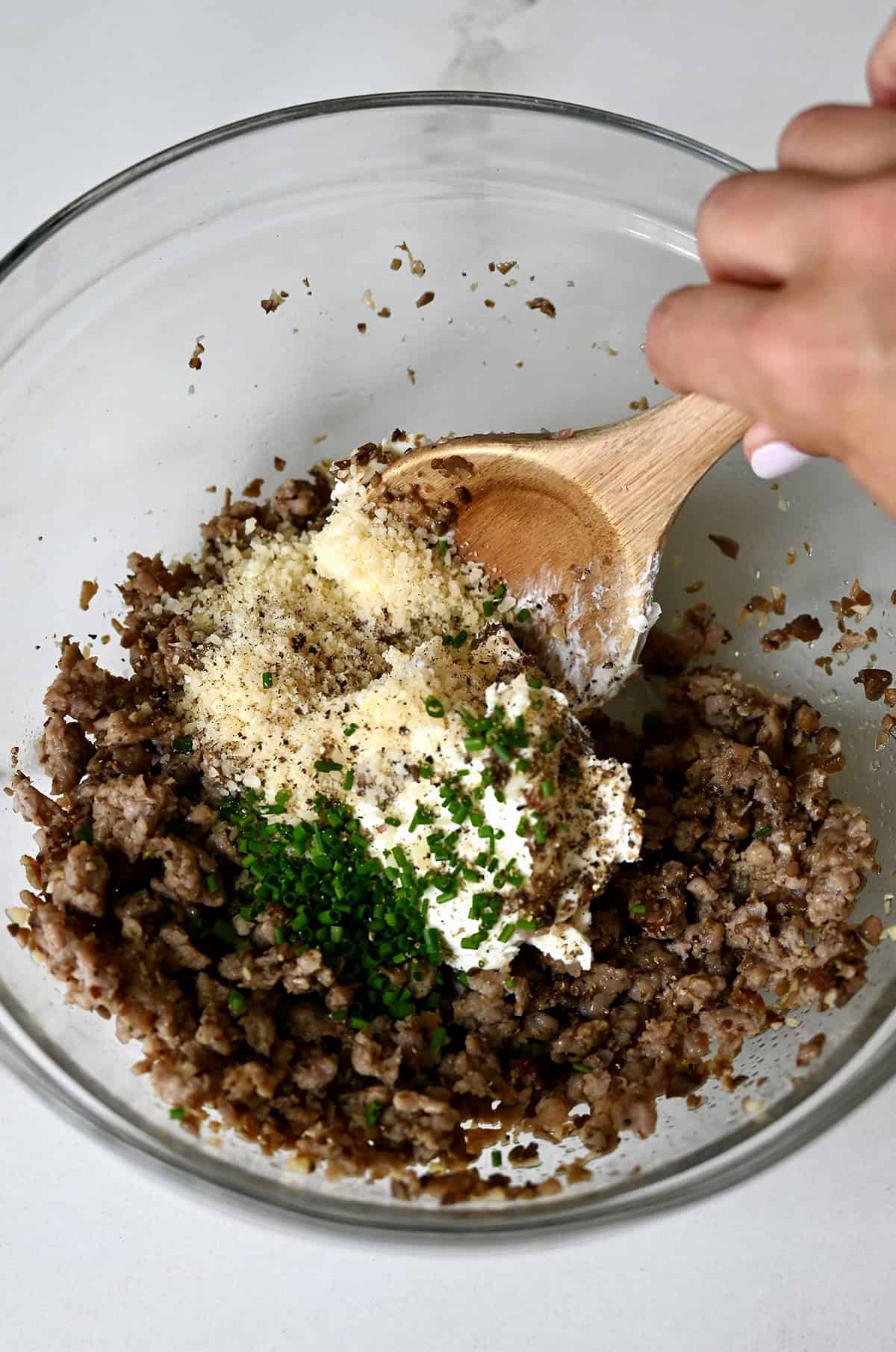 Mushroom-sausage mixture in a bowl with grated Parmesan, cream cheese and chopped fresh chives.