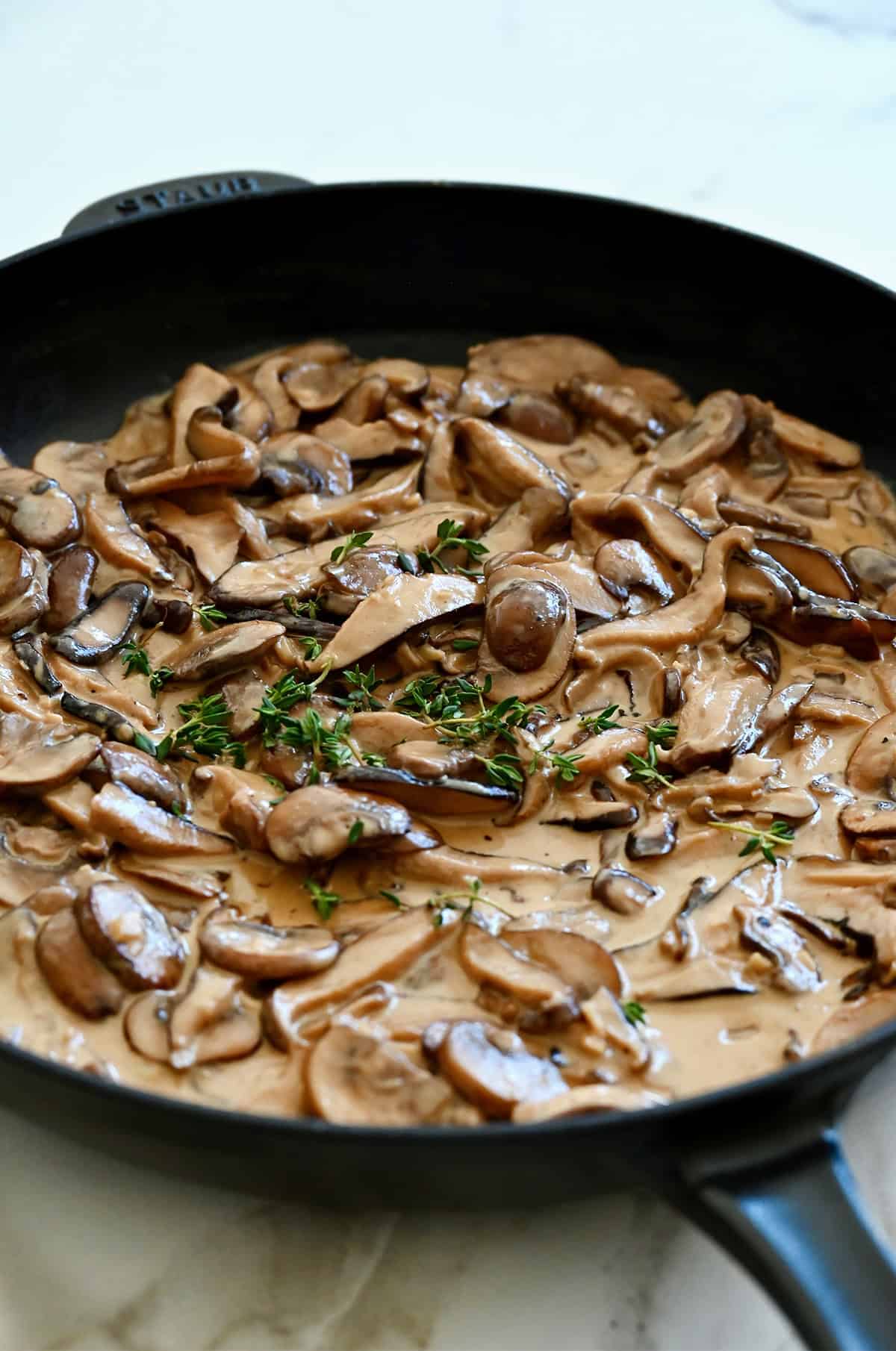 Mushroom cream sauce in a large skillet, garnished with fresh thyme leaves.