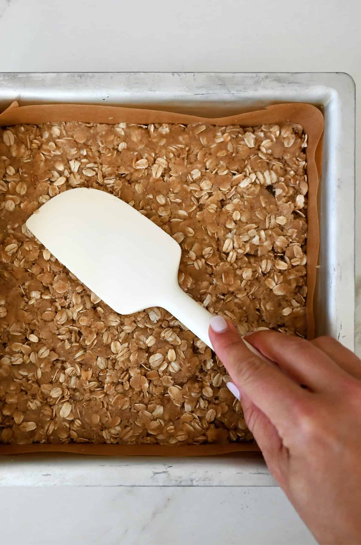 Oatmeal crust for cranberry bars in a parchment paper-lined baking dish.