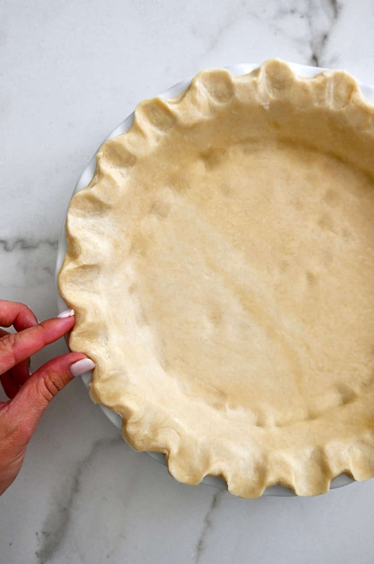 Crimping the edges of homemade pie crust in a pie pan.