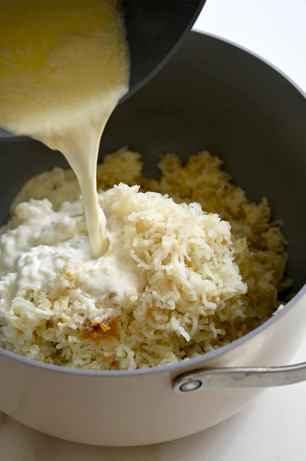 Slowly adding warmed milk and heavy cream atop mashed potatoes.