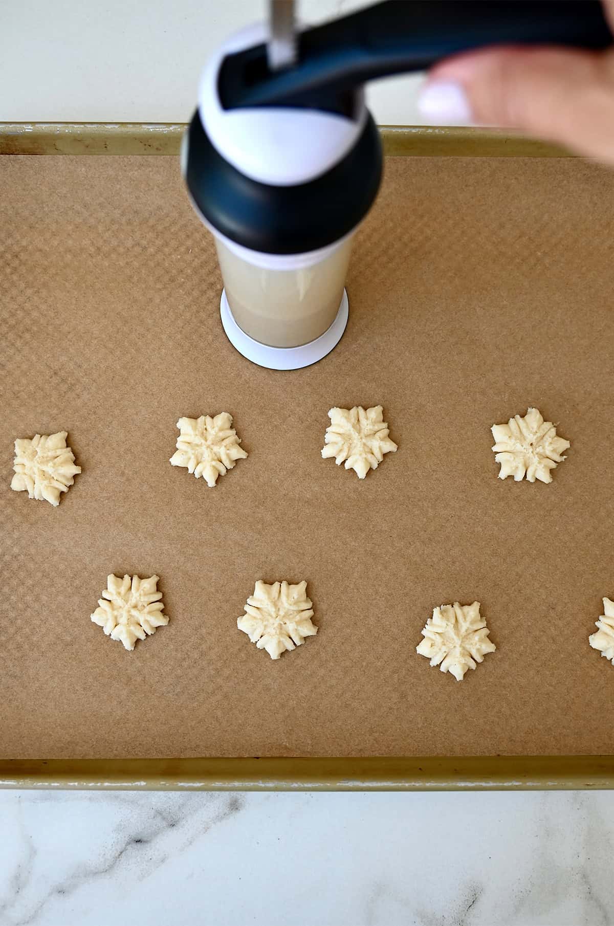 Pressing dough from a cookie press onto an unlined, ungreased baking sheet.