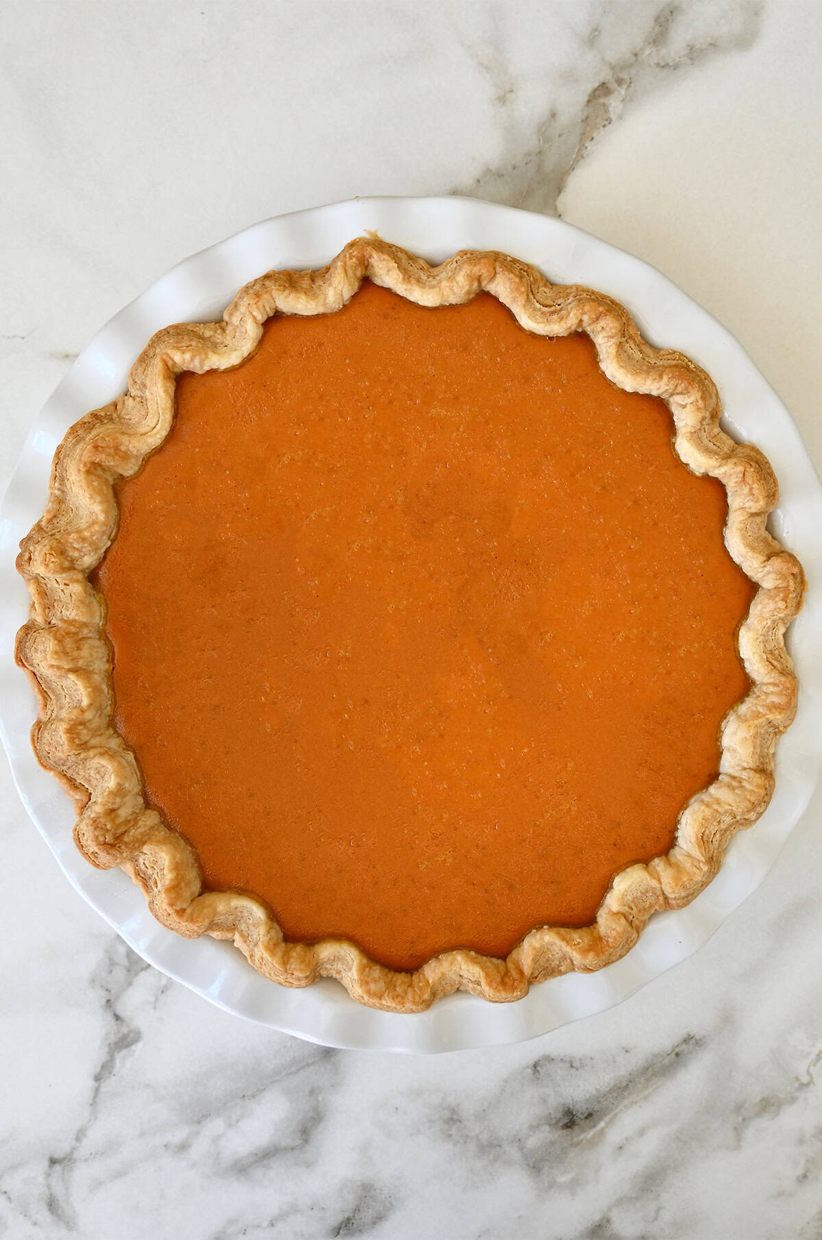 Homemade pumpkin pie without cracks, cooling on the counter.