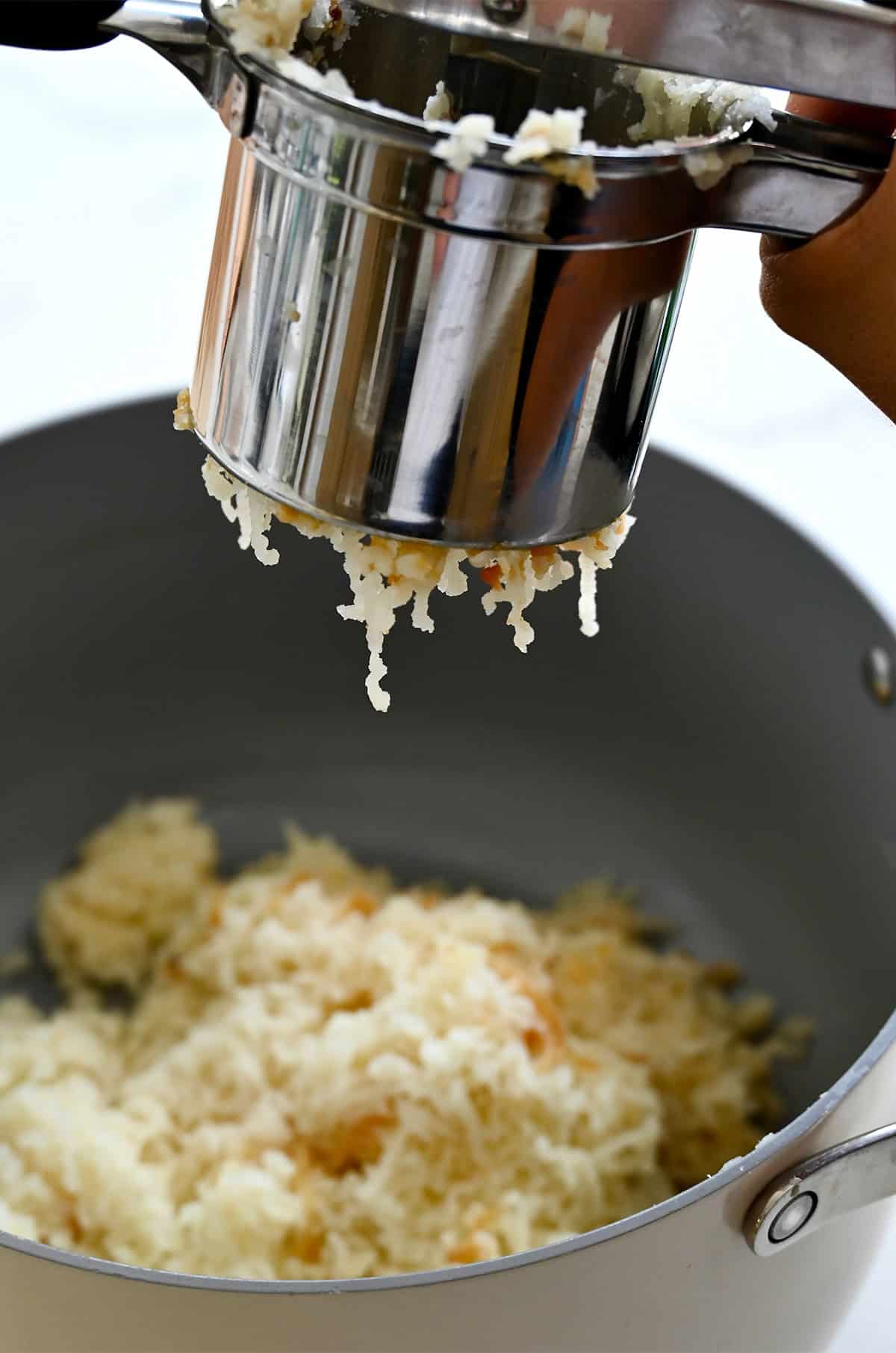 Passing boiled potatoes through a ricer for creamy mashed potatoes.