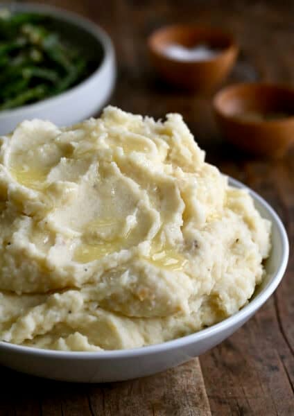 Roasted garlic mashed potatoes with melted butter in a white serving bowl.