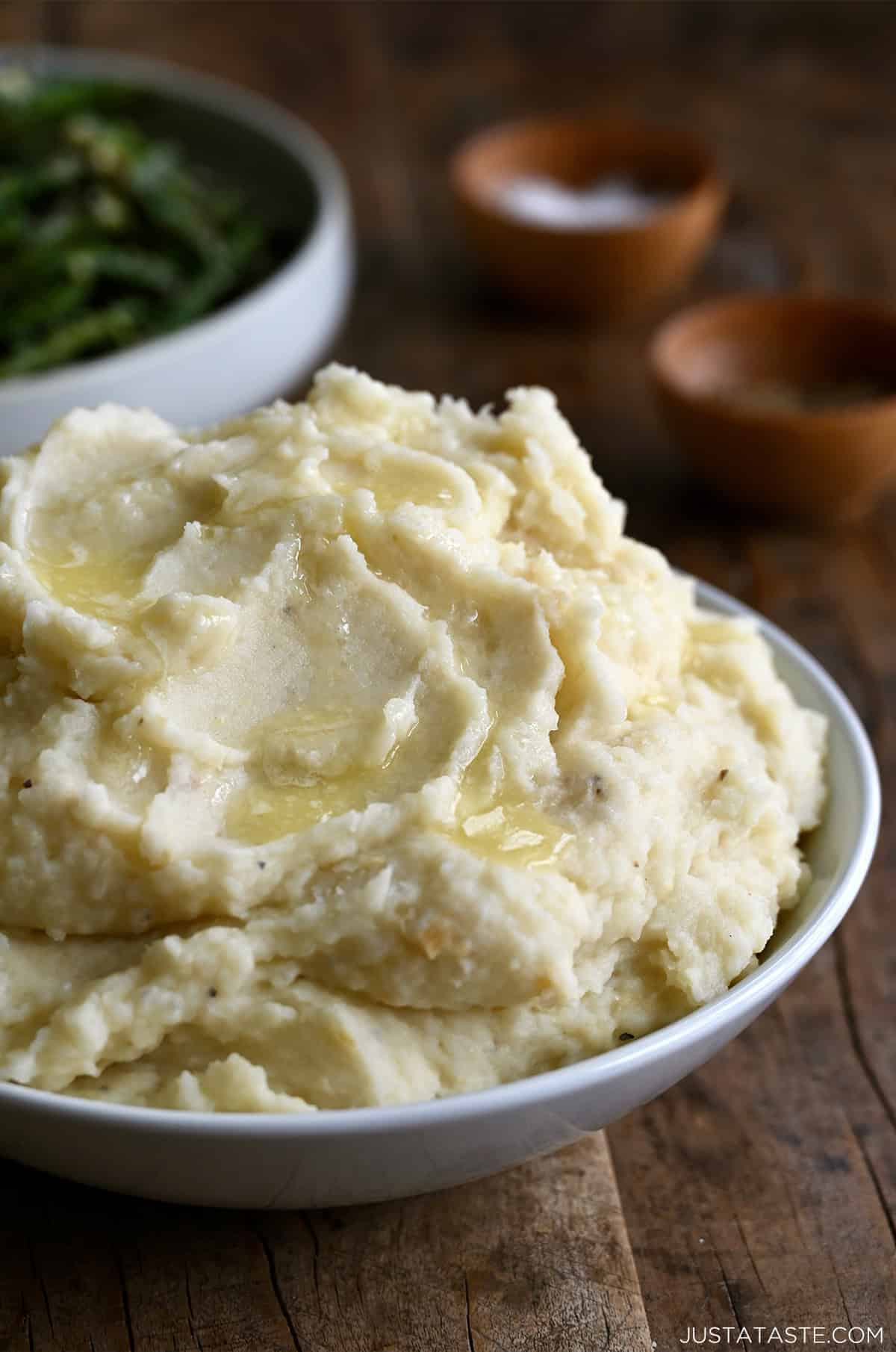 Roasted garlic mashed potatoes with melted butter in a white serving bowl.