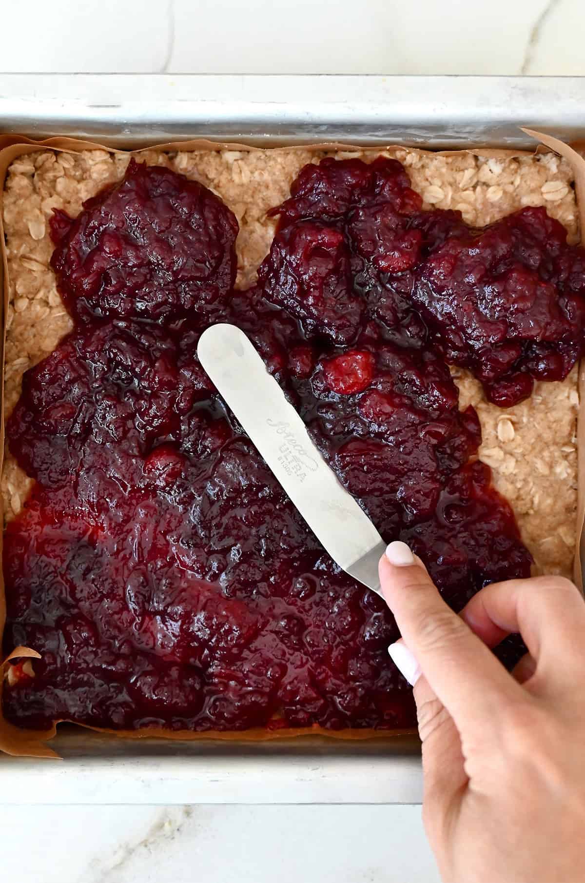 Spreading cranberry sauce over a par-baked shortbread base with an offset spatula.
