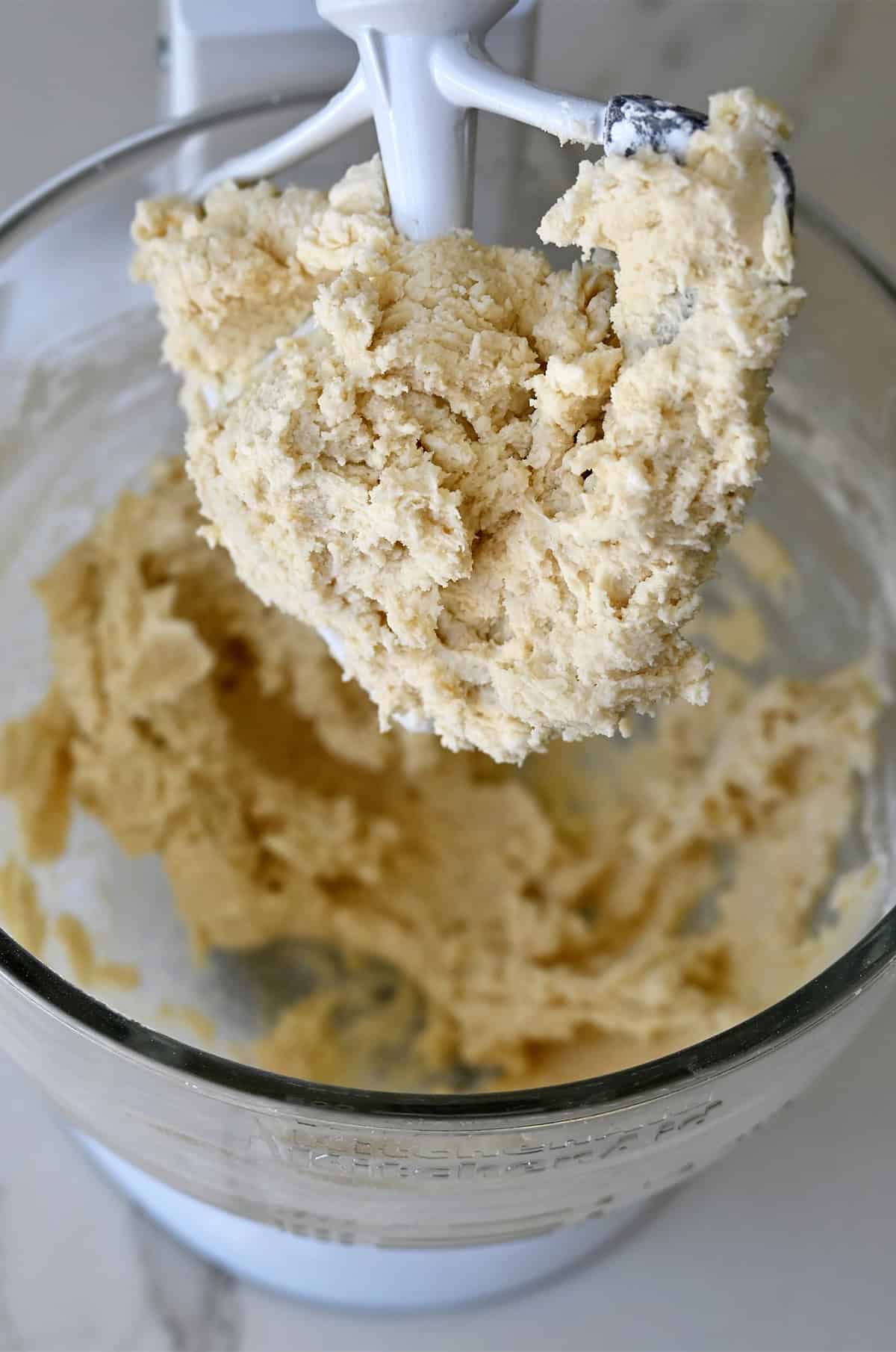 Spritz cookie dough in the bowl of a stand mixer with the paddle attachment.