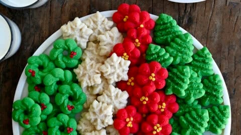 A cookie tray with a variety of traditional spritz cookies, including green Christmas trees, red rosettes, snowflakes with sprinkles, and green wreaths.
