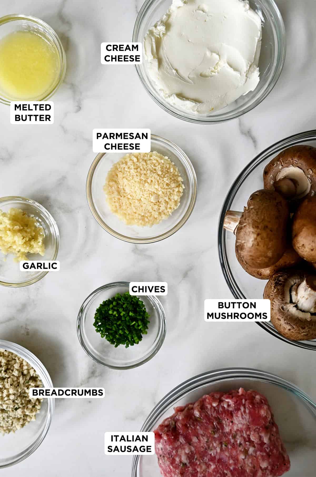 Ingredients to make stuffed mushrooms with sausage in various sizes of glass bowls.