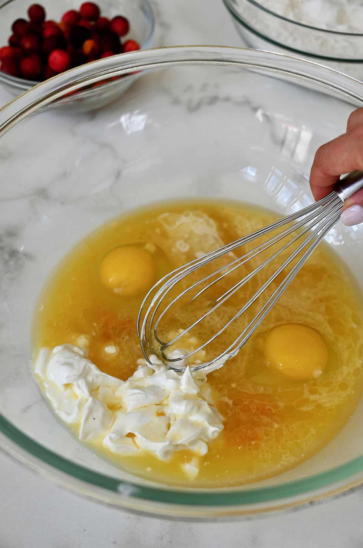 Orange juice, eggs, sour cream, orange zest and vanilla extract being whisked together in a bowl.