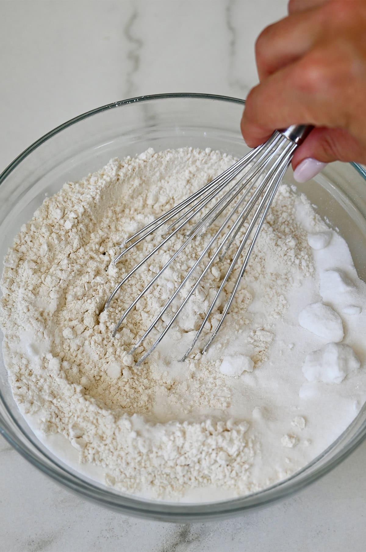 Dry ingredients for cranberry muffins in a glass bowl with a whisk.