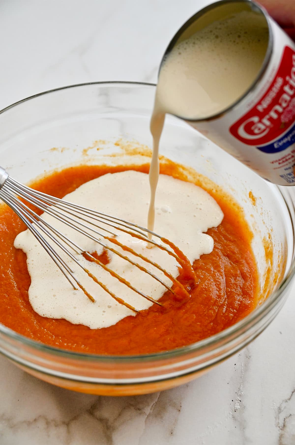 Whisking evaporated milk into a mixture of pumpkin puree, spices and eggs to make pumpkin pie filling.