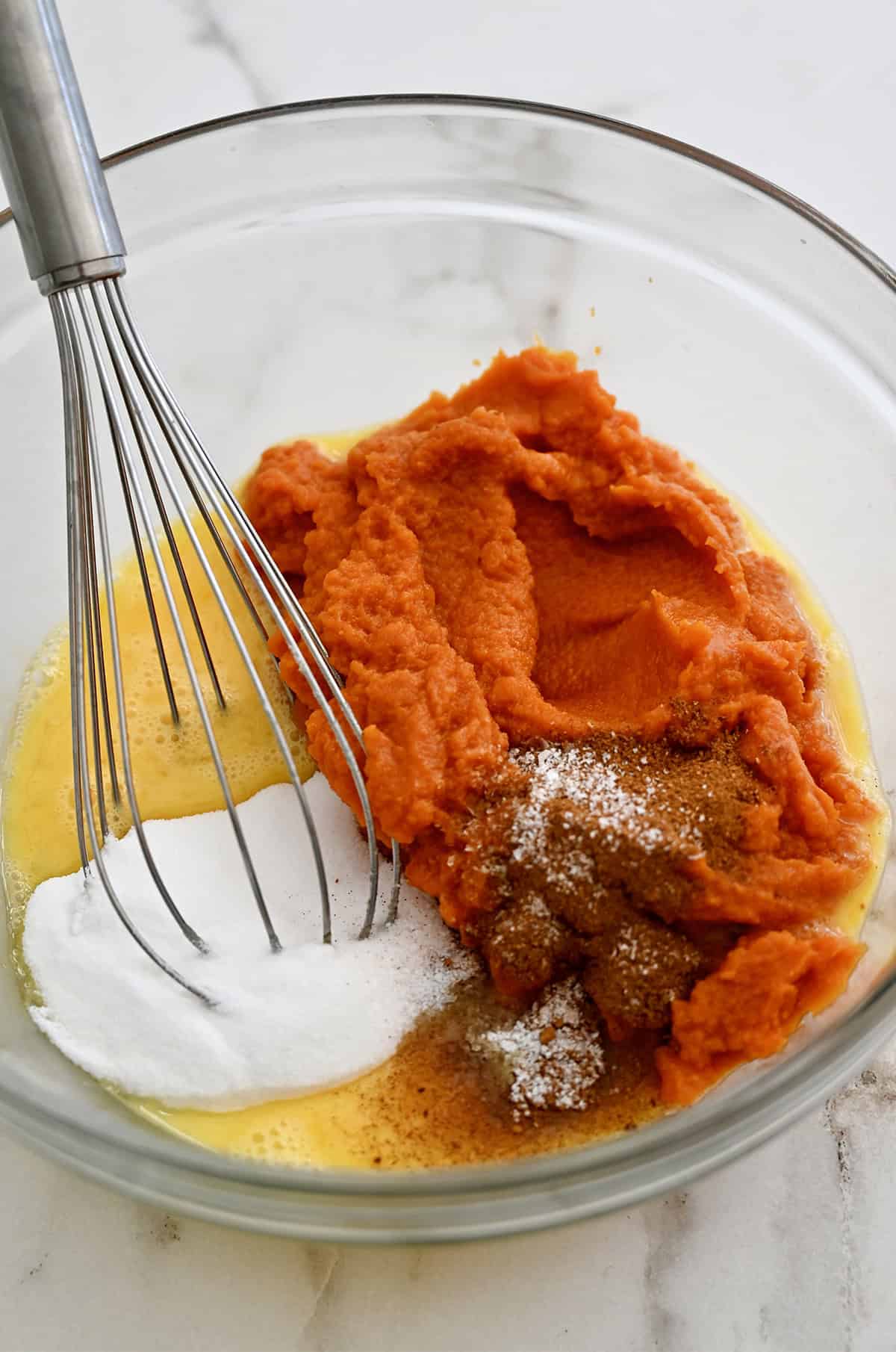 A glass bowl containing pumpkin puree, pumpkin spice, sugar, salt and eggs.