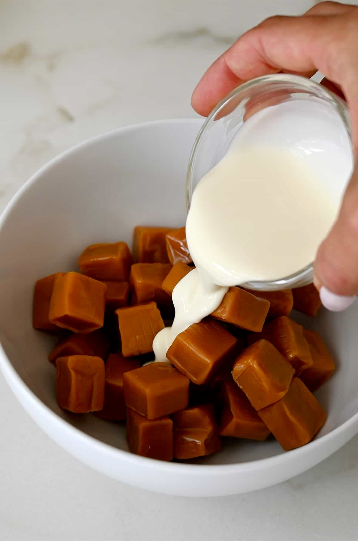 Adding heavy cream to a bowl with soft store-bought caramels.