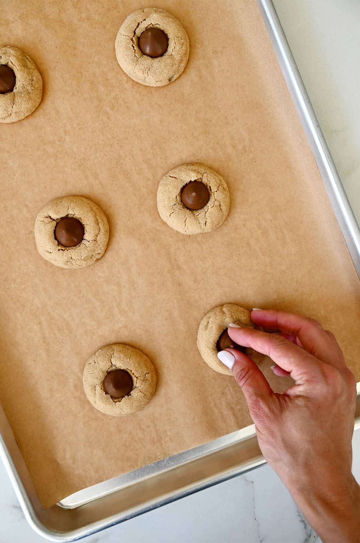 Pressing a chocolate kiss into warm peanut butter cookies to make peanut butter blossoms.