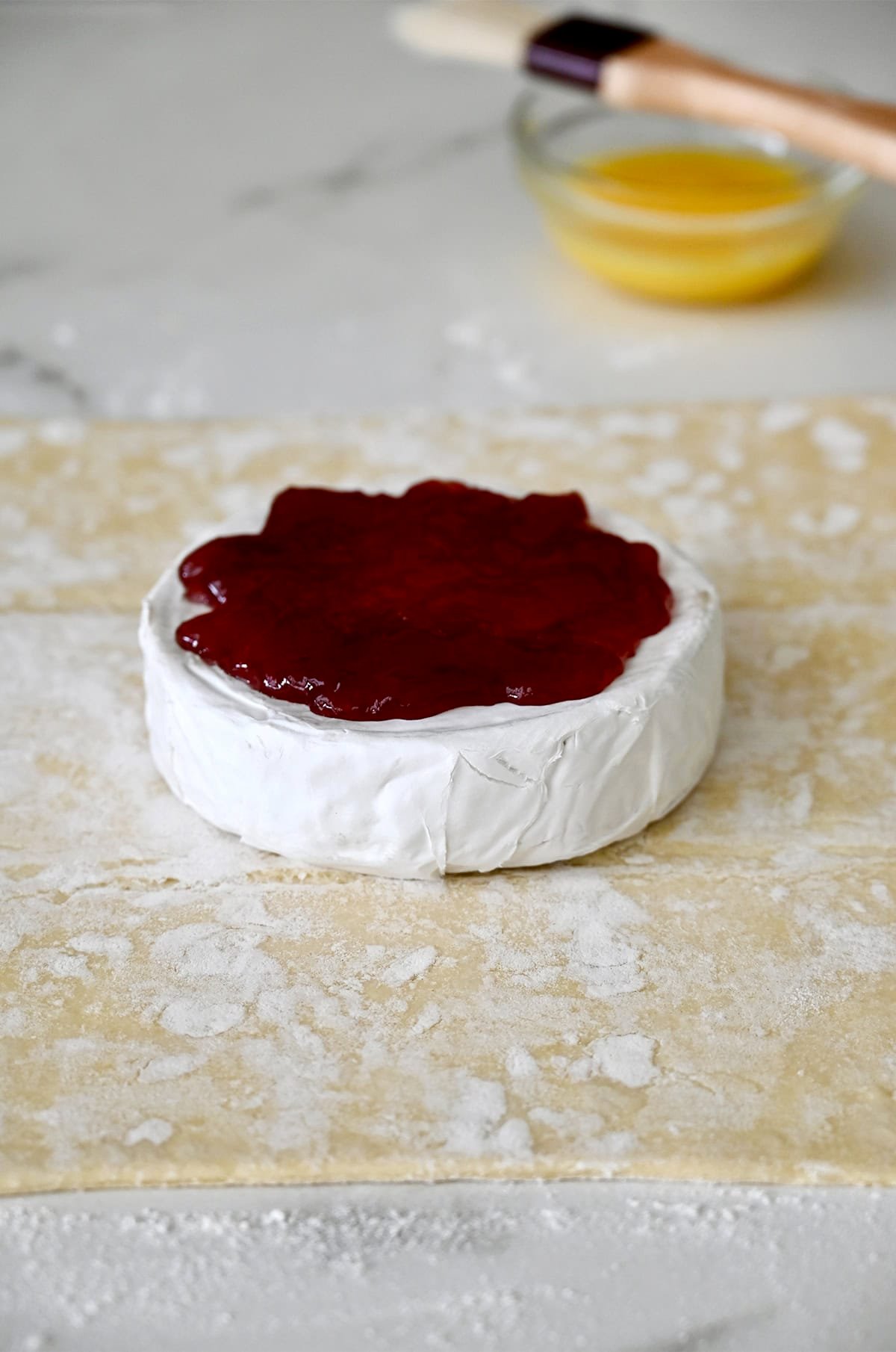 A wheel of Brie cheese topped with jam in the center of a puff pastry sheet.