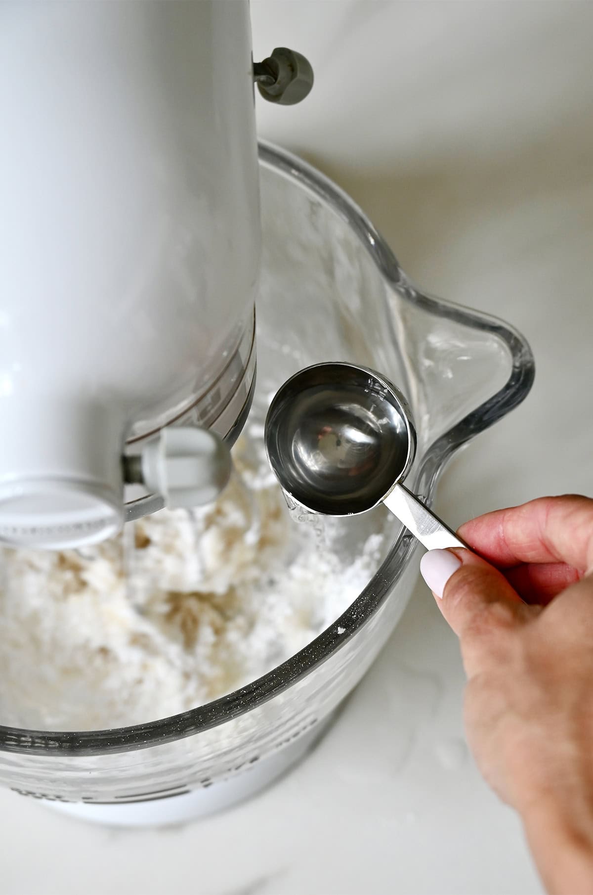 Adding warm water to a stand mixer bowl with powdered sugar and meringue powder to make royal icing.