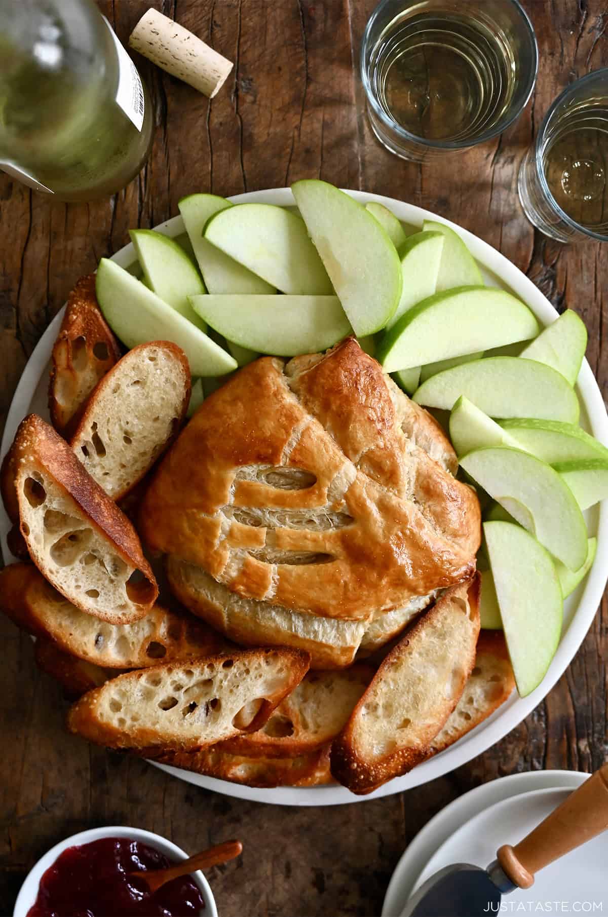 Baked puff pastry Brie on a serving platter surrounded by apple slices and toasted baguette slices.