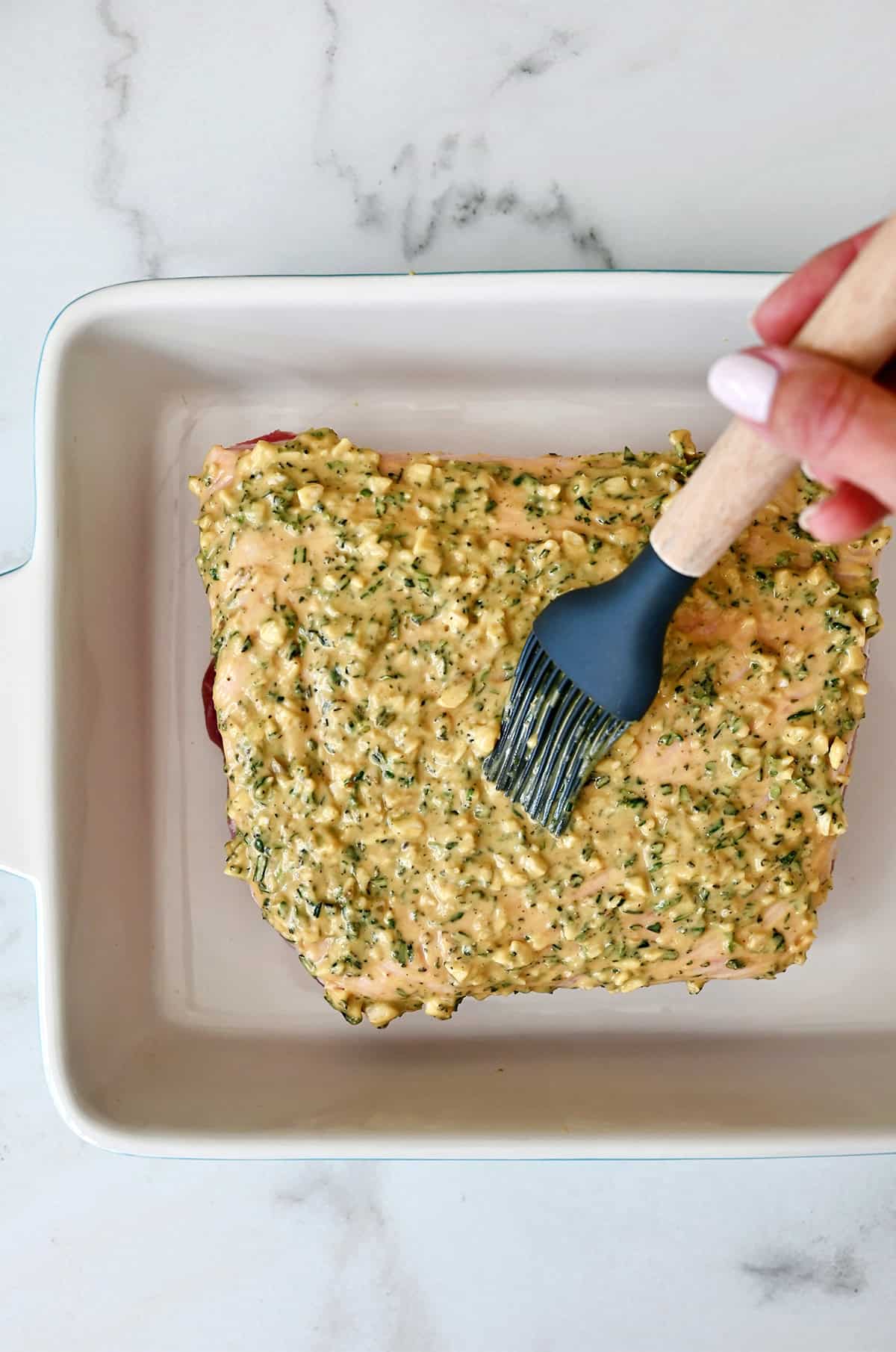 Slathering on Dijon mustard and herbs on top of a pork loin for roasting.