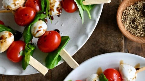 Caprese skewers with balsamic glaze, olive oil drizzle, sea salt and ground black pepper on a serving plate.