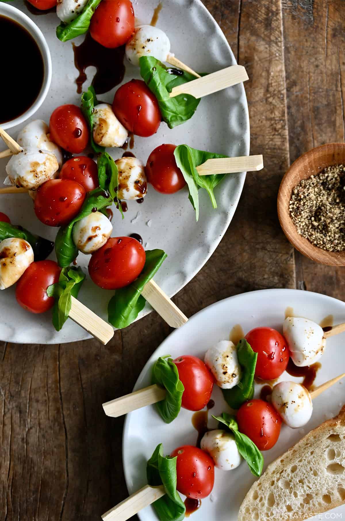 Caprese skewers with balsamic glaze, olive oil drizzle, sea salt and ground black pepper on a serving plate.