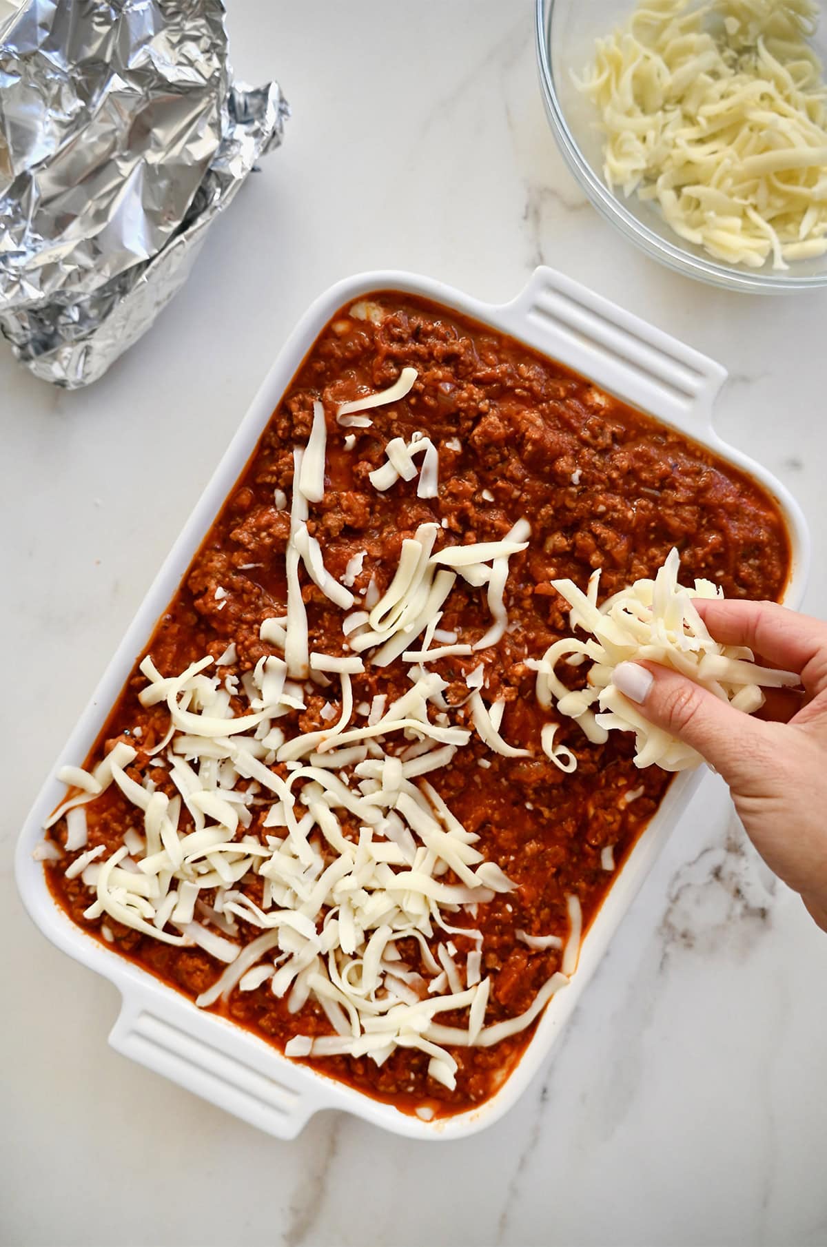 Lasagna with layers of marinara sauce, pasta, and a cottage cheese filling, topping with shredded mozzarella before going into the oven.