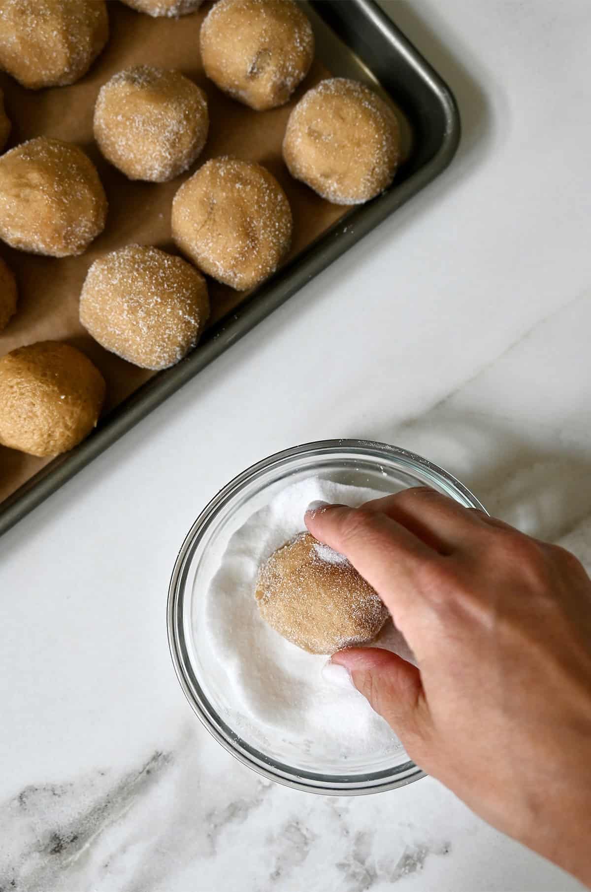 Rolling peanut butter dough balls in granulated sugar.